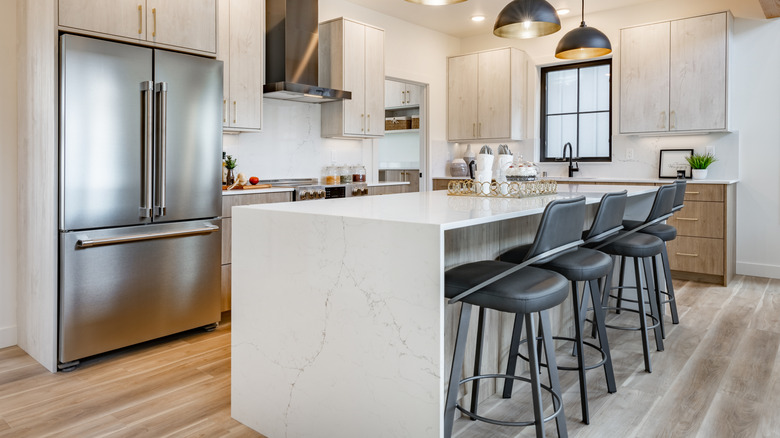 A beautiful kitchen with a white marble-look island bench, complete with four black stools