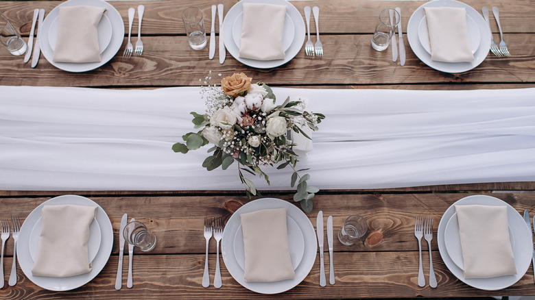 A set table with a white runner and flowers in the center