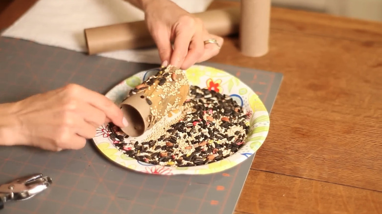 A woman making a bird feeder with seed and a roll paper tube
