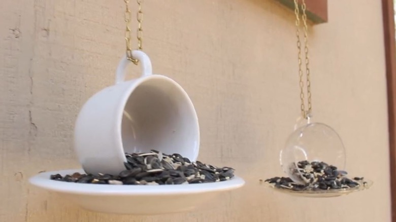 two DIY teacup bird feeders hanging while filled with seeds