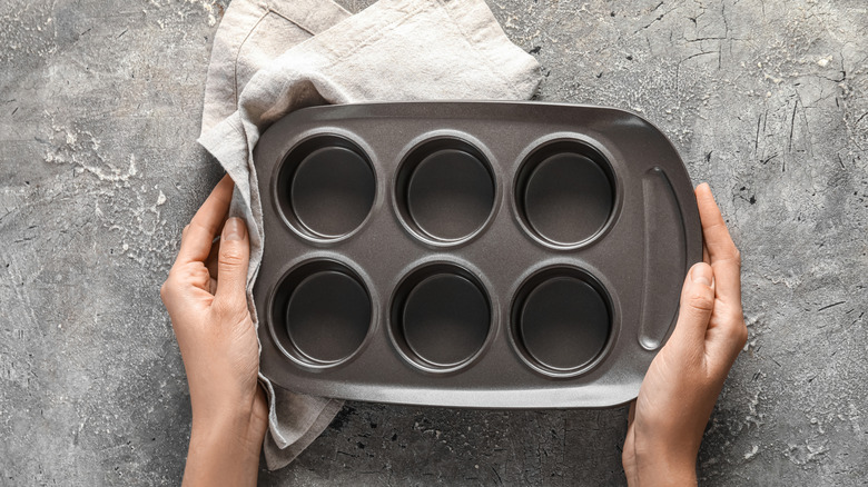 person's hands holding muffin pan