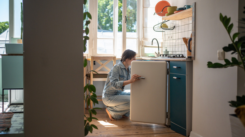 A person peering into a mini fridge