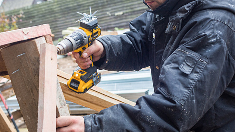 Worker wearing protective gear using a DeWalt drill to screw some wood pieces together.