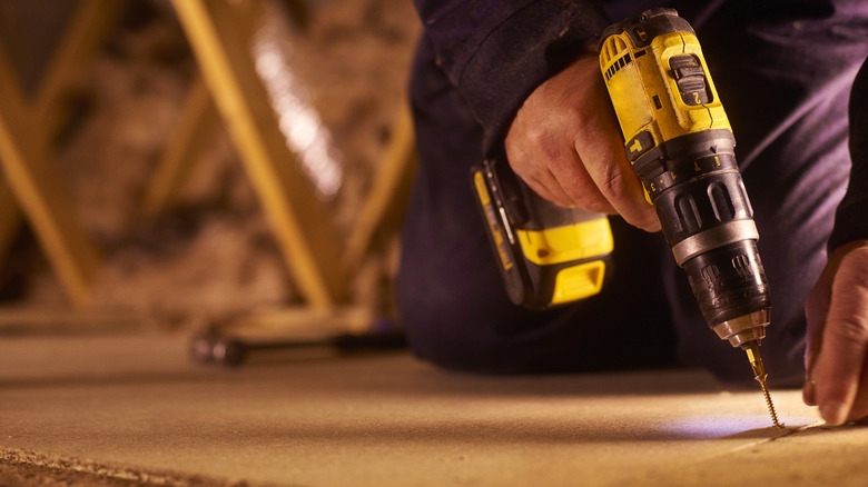 A carpenter is using a Dewalt cordless drill to drill the screws into the floorboard to secure it to the the roof joist.