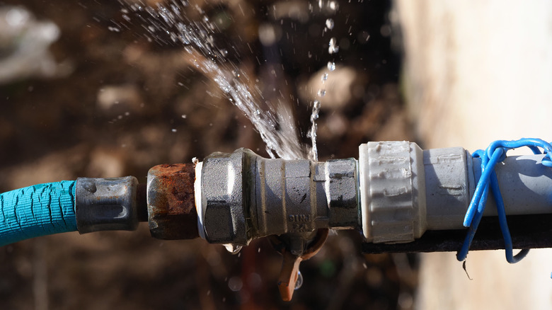 A frozen pipe connector has cracked, leading to a spray of water.