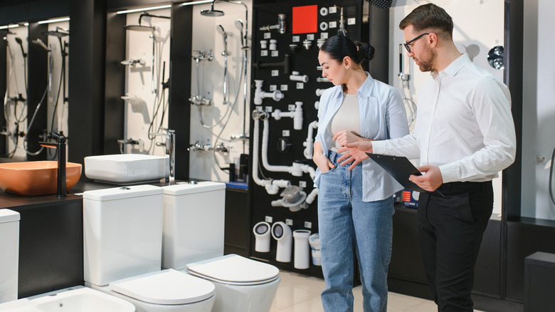 Salesman assisting a woman as she browses toilets in a store
