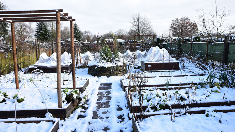 A fenced yard filled with raised beds is covered in heavy layers of snow.