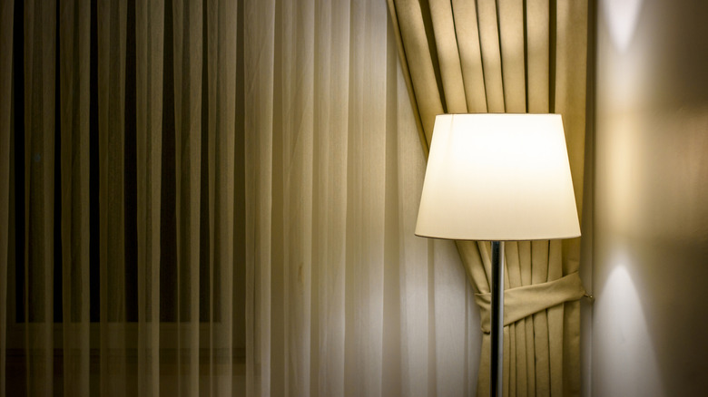 Tall standing lamp in a room with the curtains closed