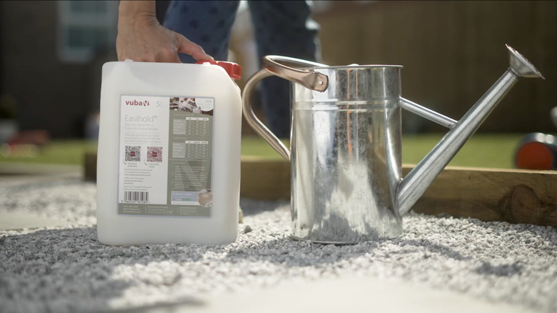 A person sets a container of Easihold landscape rock glue next to a metal watering can