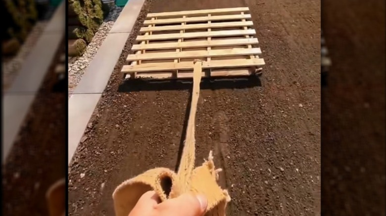 Person dragging a wood pallet to level soil
