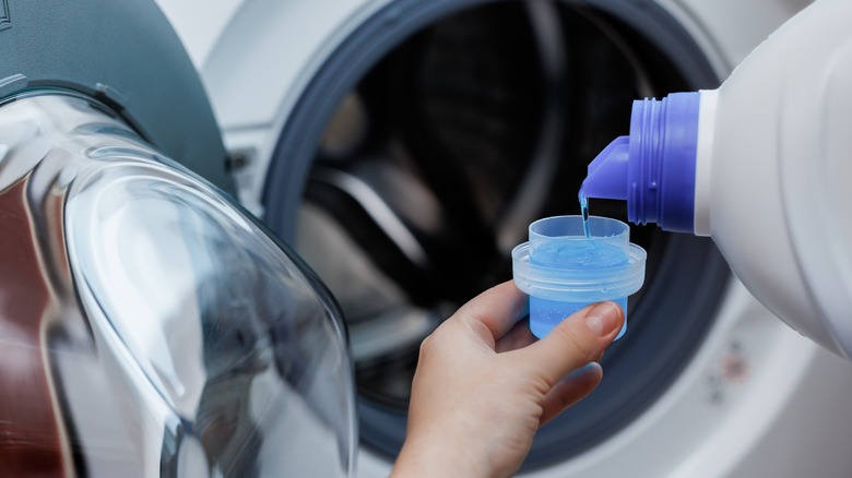 person measuring liquid laundry detergent