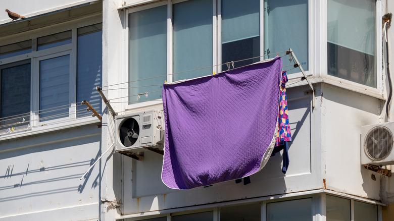 A white and purple blanket air drying from a clothesline outside an apartment