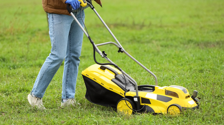 A person using a yellow and black mower to cut grass