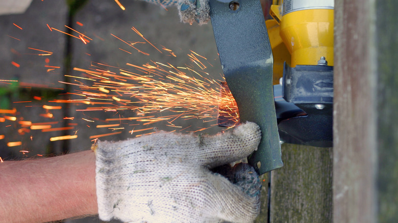 A person sharpening a lawn mower blade on a grinder