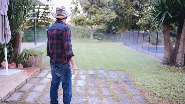 A man stands on his concrete block patio contemplating what to do with his lawn in his backyard.
