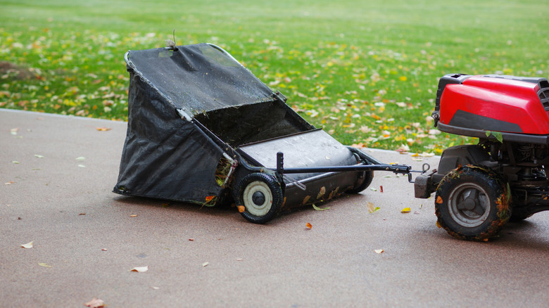 A lawn sweeper on a driveway next to a yard with strewn leaves