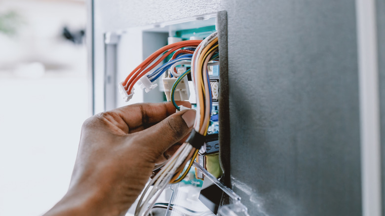 A person accesses the electrical wires in a wall.