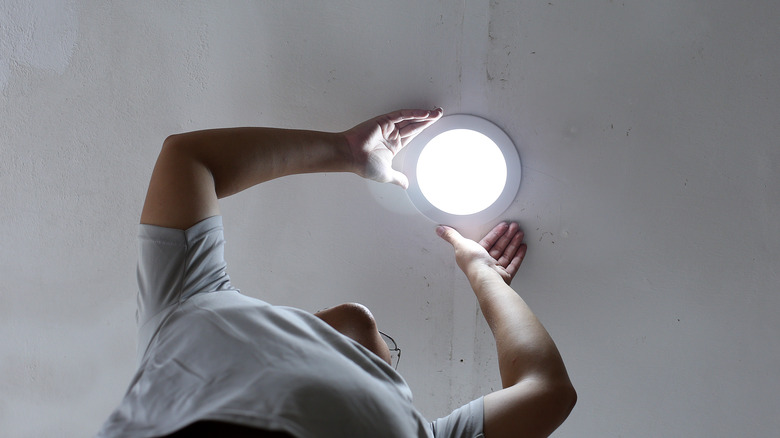 A man installs a can LED ceiling light in a finished ceiling.