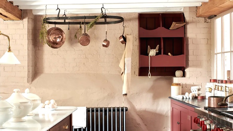Beautiful rustic kitchen with maroon cabinets, black, and white countertops, and a blackened steel pot rack hanging from the ceiling.