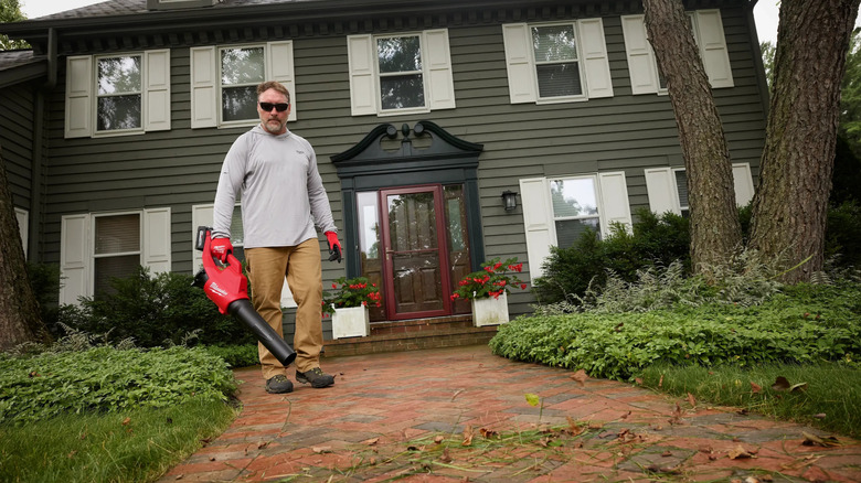 A person clearing their brick pathway with Milwaukee's M18 120 MPH 450 CFM Cordless Brushless Handheld Battery Powered Leaf Blower