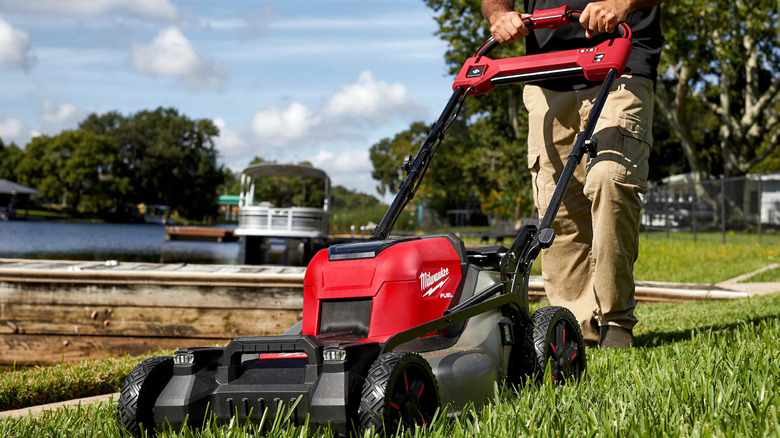 A person mowing a lawn with Milwaukee's M18 Brushless Cordless 21-inch Dual Battery Walk-Behind Self-Propelled Mower