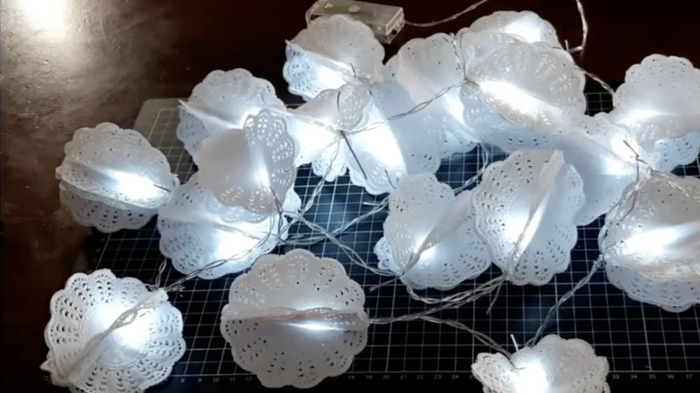 Paper lanterns made from doilies attached to each bulb on a strand of string lights.