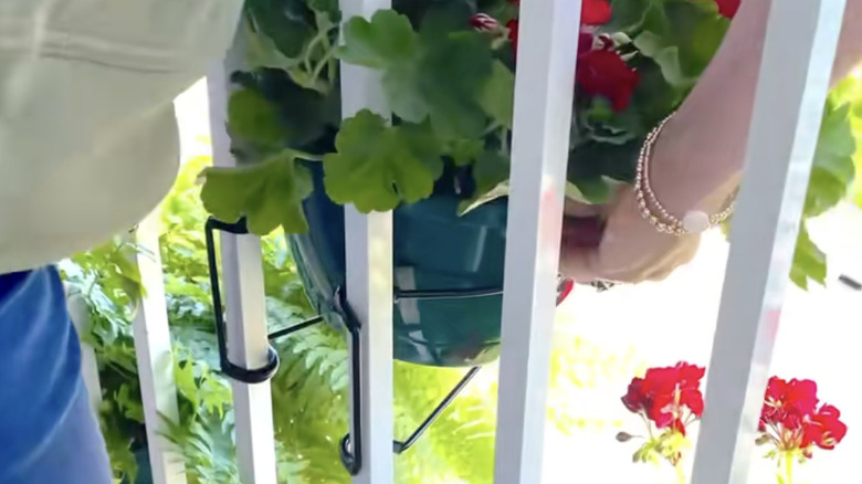 Hands hooking a railing clip to a railing to hold a flower pot.