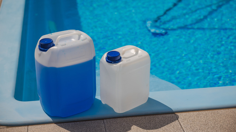 Two plastic chemical canisters with blue caps placed on the edge of a swimming pool, used for water treatment and maintenance in bright sunlight.