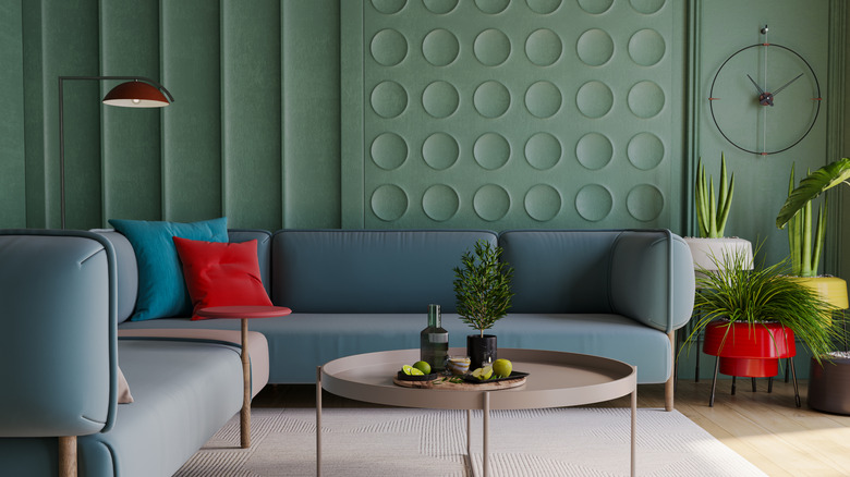 A color-drenched living room with green walls, a blue sofa and a beige round coffee table