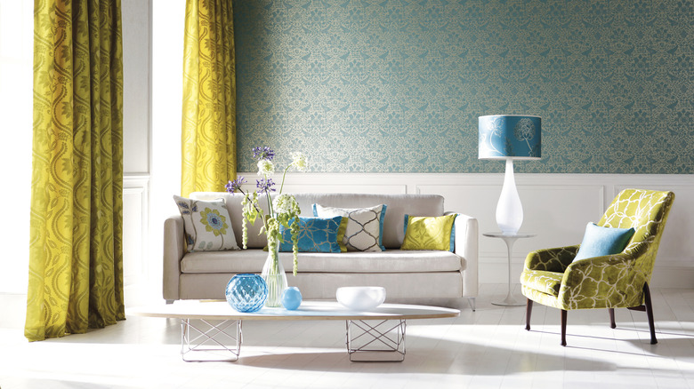 A living room with green/blue wall paper and long yellow curtains and a white sofa and green accent chair