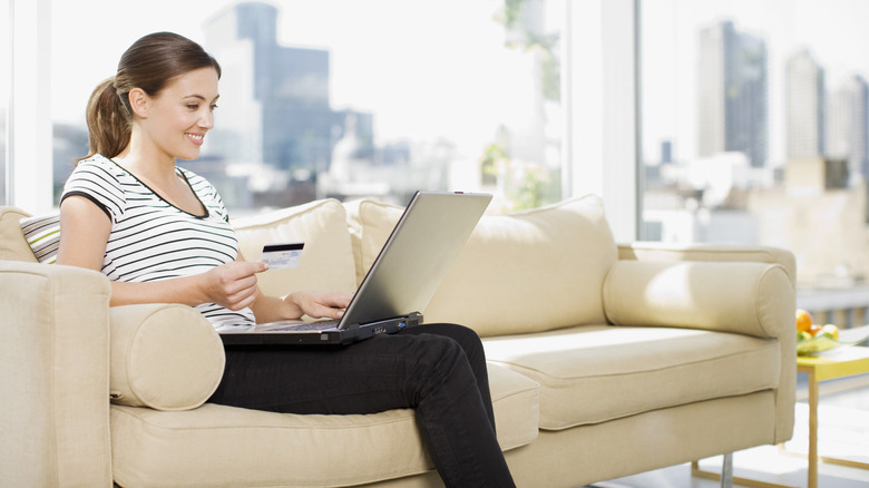 A person sitting on a sofa and shopping online with their laptop and a credit card