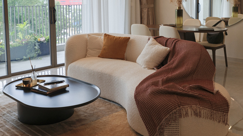 A living room with curvy sofa, table, mirrors, and more