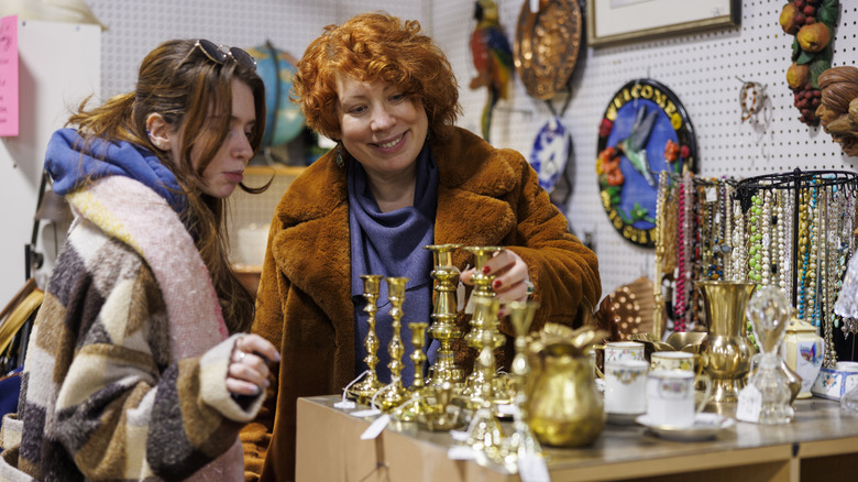 Two women admire brass candlesticks in a secondhand store.