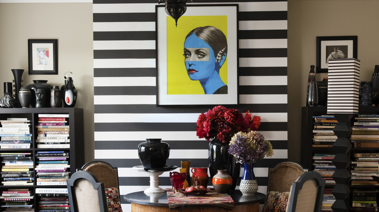 Eclectic maximalist dining room with black and white striped accent wall, black bookshelves and black decor, matching patterns.