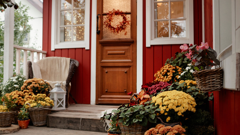 Front porch of a red house with baskets of mums and a wicker chair.