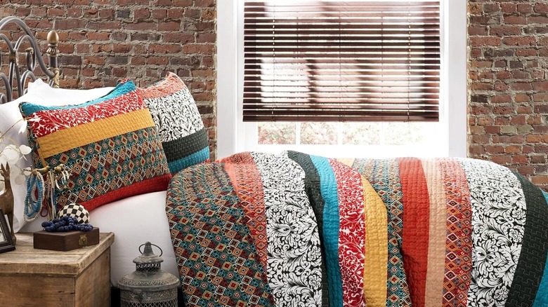 A brightly colored striped quilt offers a boho vibe in a bedroom with a brick wall