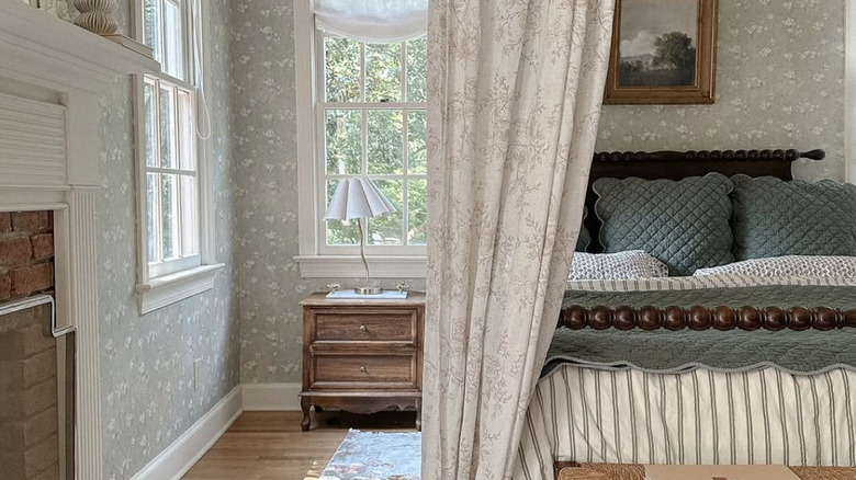 A traditional bedroom with floral wallpaper, toile bed curtains, and striped bedding