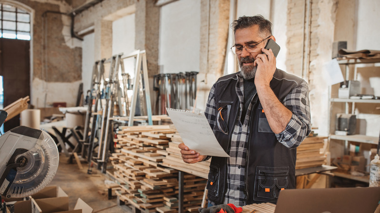 Carpenter in workshop, on phone and looking at piece of paper