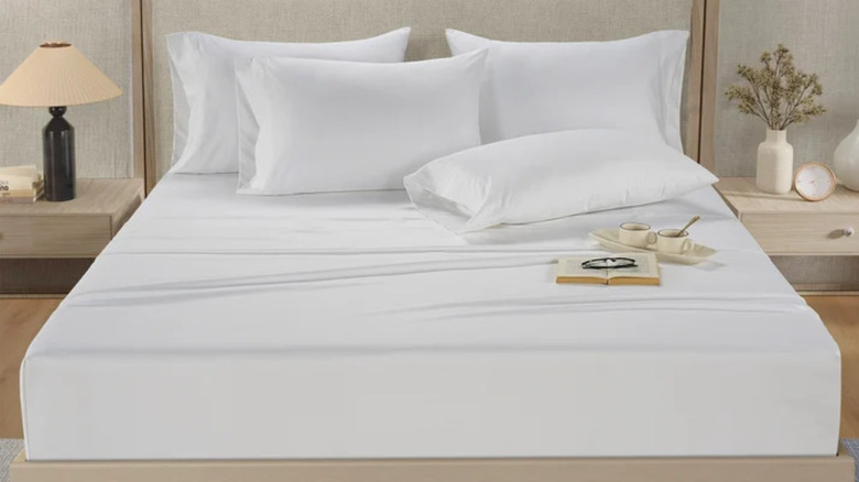 A plush white bed with fluffed pillows and two cups of tea.