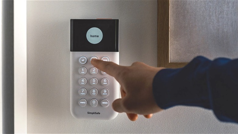 Person's hand pushing buttons on SimpliSafe home security system.