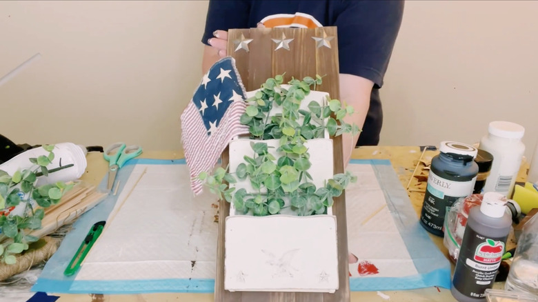 wall-mounted mail holder on craft table, filled with eucalyptus leaves and an American flag