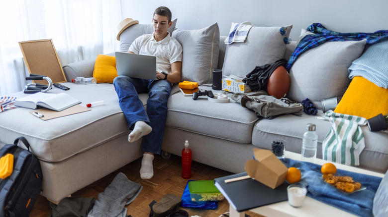 Person sitting on couch surrounded by clutter