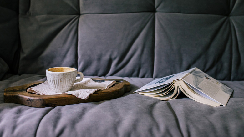 An image of an upside down book and a coffee cup and napkin on a wooden sofa tray.