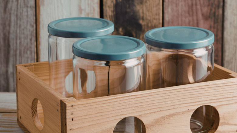 Three empty glass jars with metal lids sit inside a wooden crate.