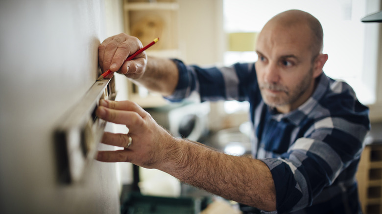 A man marking out a level space on a wall inside a home