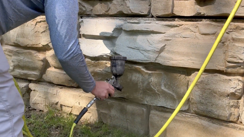 A man sprays stain on concrete block retaining wall.