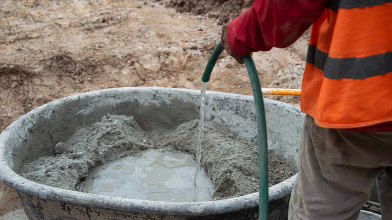 Workers are adding water to mix cement in a mixing tank.