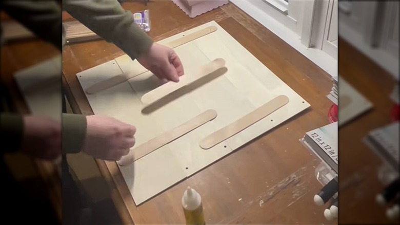 A pair of light skinned hands glue craft sticks to the back of Dollar Tree wood signs to connect them into one unit.
