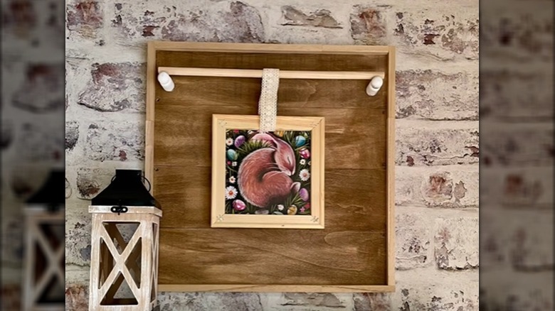 A completed wooden framed wall art piece hangs against a painted brick wall.