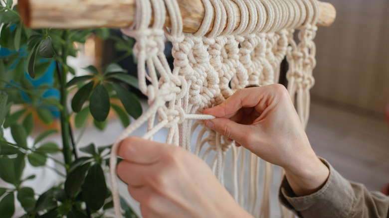 A woman weaving and tying rope to create a macrame pattern